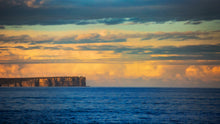Load image into Gallery viewer, Soft afternoon light illuminates the distant cliffs and clouds across the bay's blue waters. Jervis Bay, NSW.