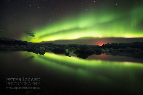 Jökulsárlón, Iceland, whilst I waited and composed this shot, the orange glow of an erupting inland volcano began to put on a show, around midnight during an aurora light spectacular. Peter Izzard Photography Fine Art Print.